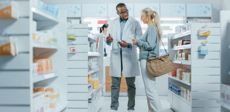 "A A pharmacist holding a medicine box speaking to a patient in a pharmacy.
