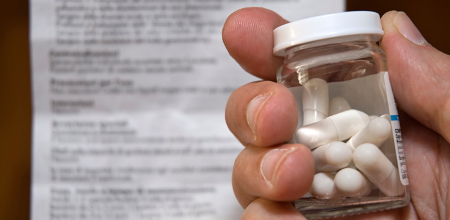 "Patient Patient holding a medicine bottle filled with tablets. A product information leaflet is blurred in the background.